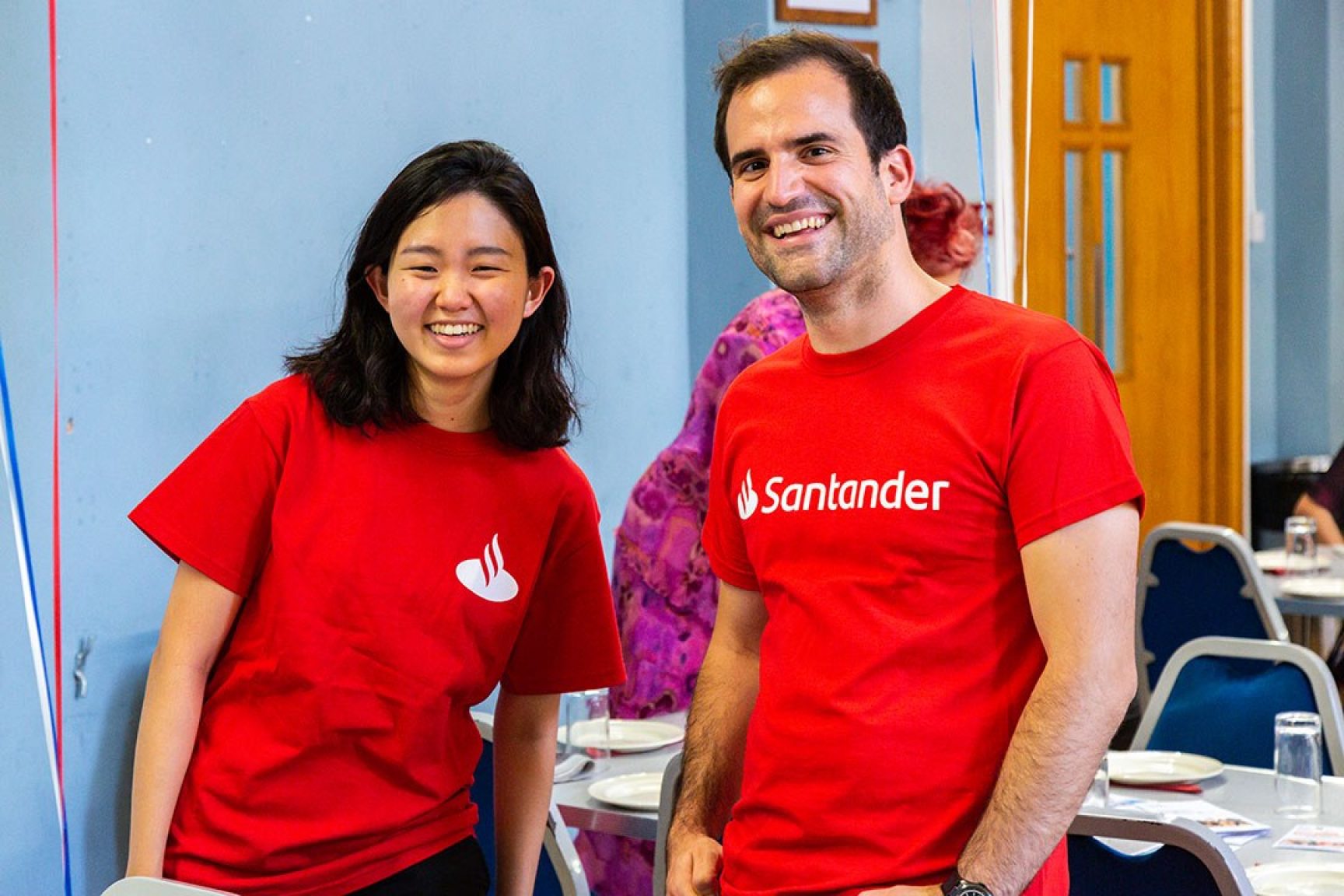Two volunteers wearing Santander tshirts at a community event. They are smiling at the camera and having a good time.