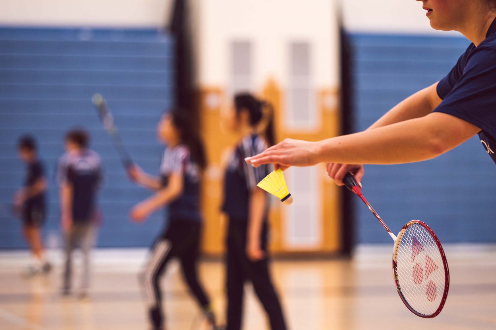 A person about to take aim and serve in a badminton game. There are other games of badminton happening in the background.